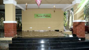 Entrada de un hotel con un letrero que dice "Areca Palms", un piso de baldosas y un conjunto de escalones de mármol negro que conducen a la entrada.