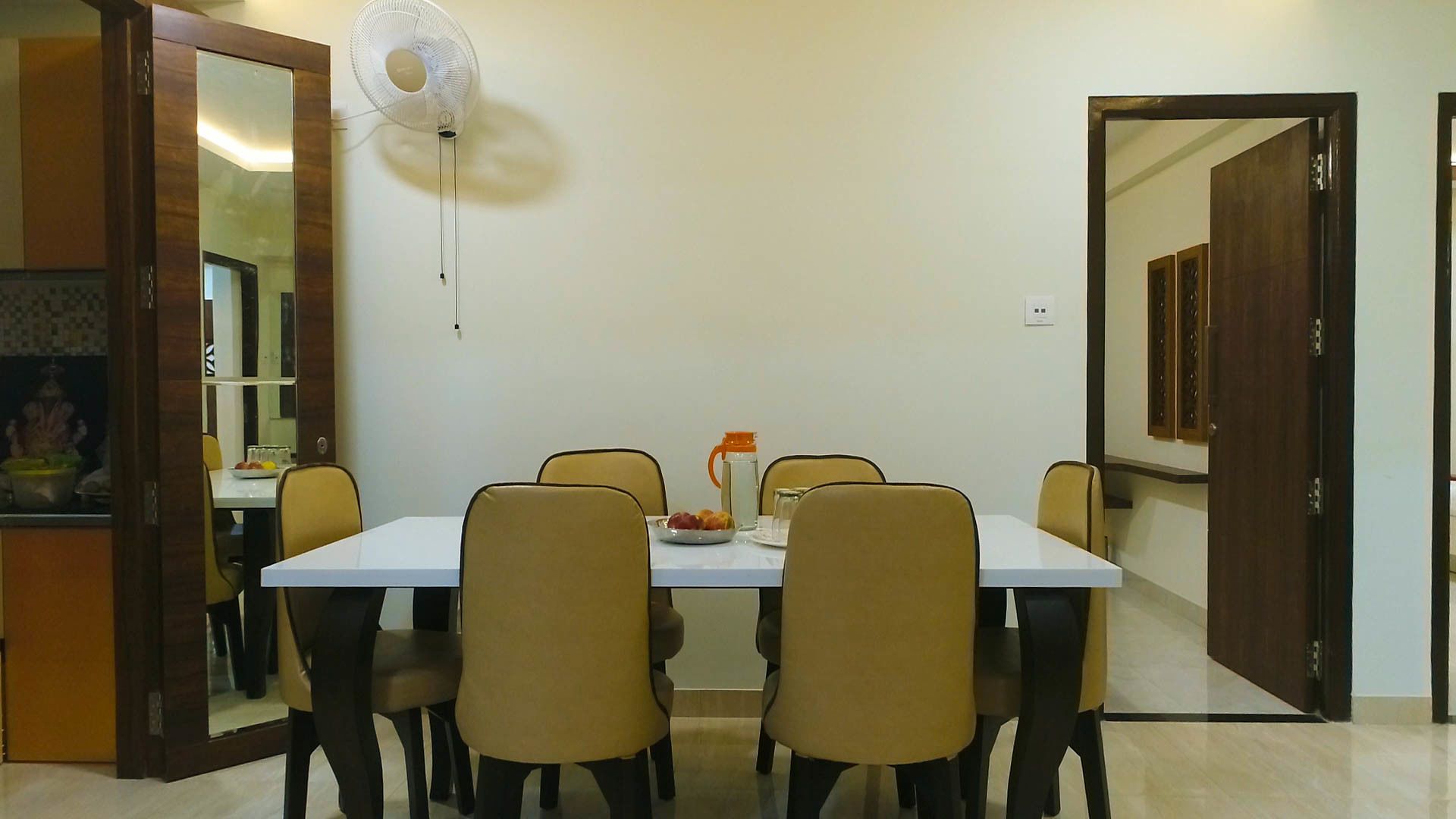 A dining area with a white table, six chairs, and a fan.