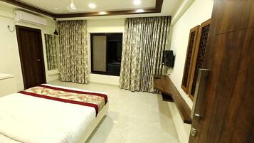 A hotel room with a bed, curtains, a TV, and a wardrobe.