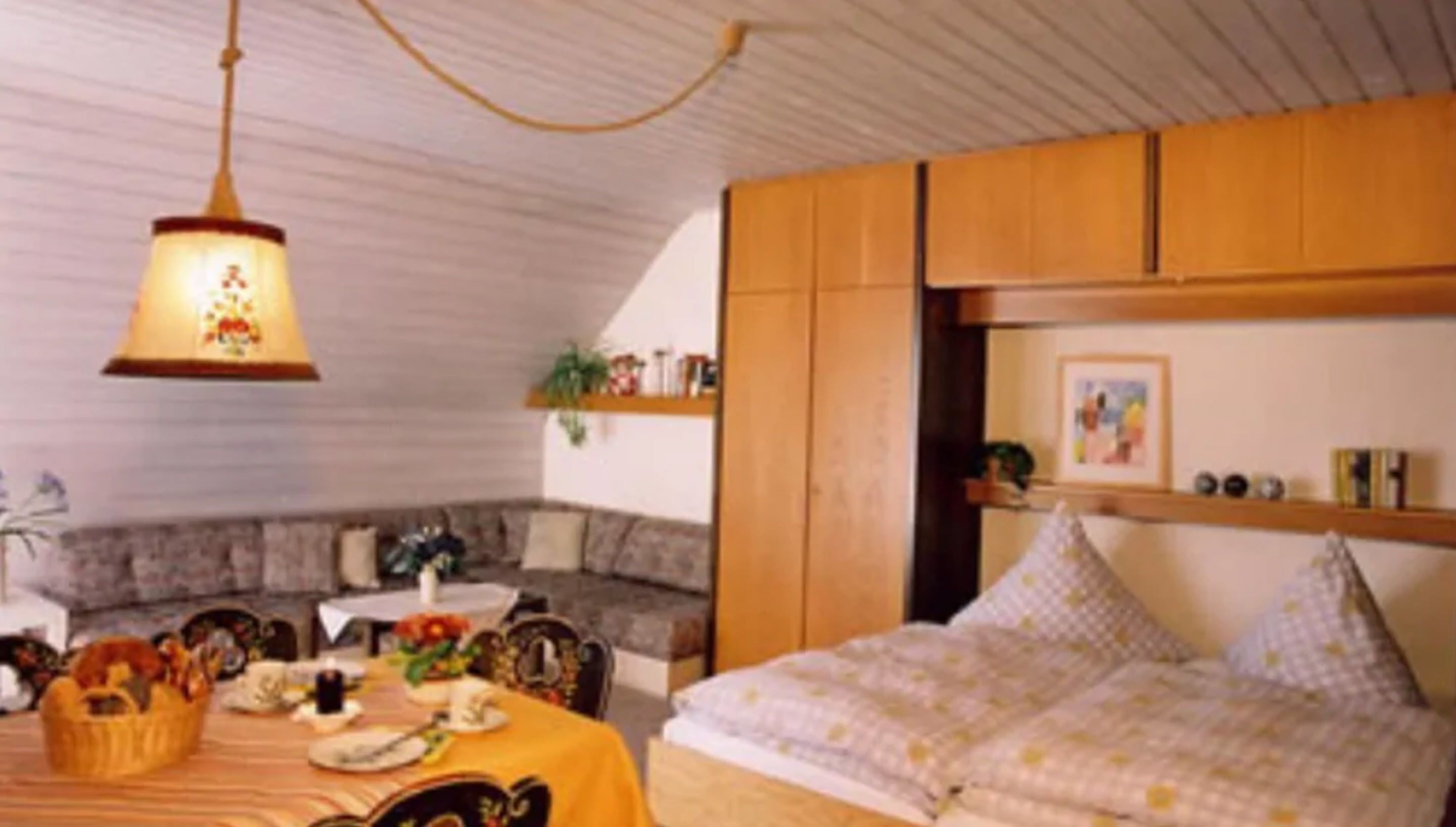 A cozy room with a dining table set for two, a sofa, and a bed with a patterned bedspread.