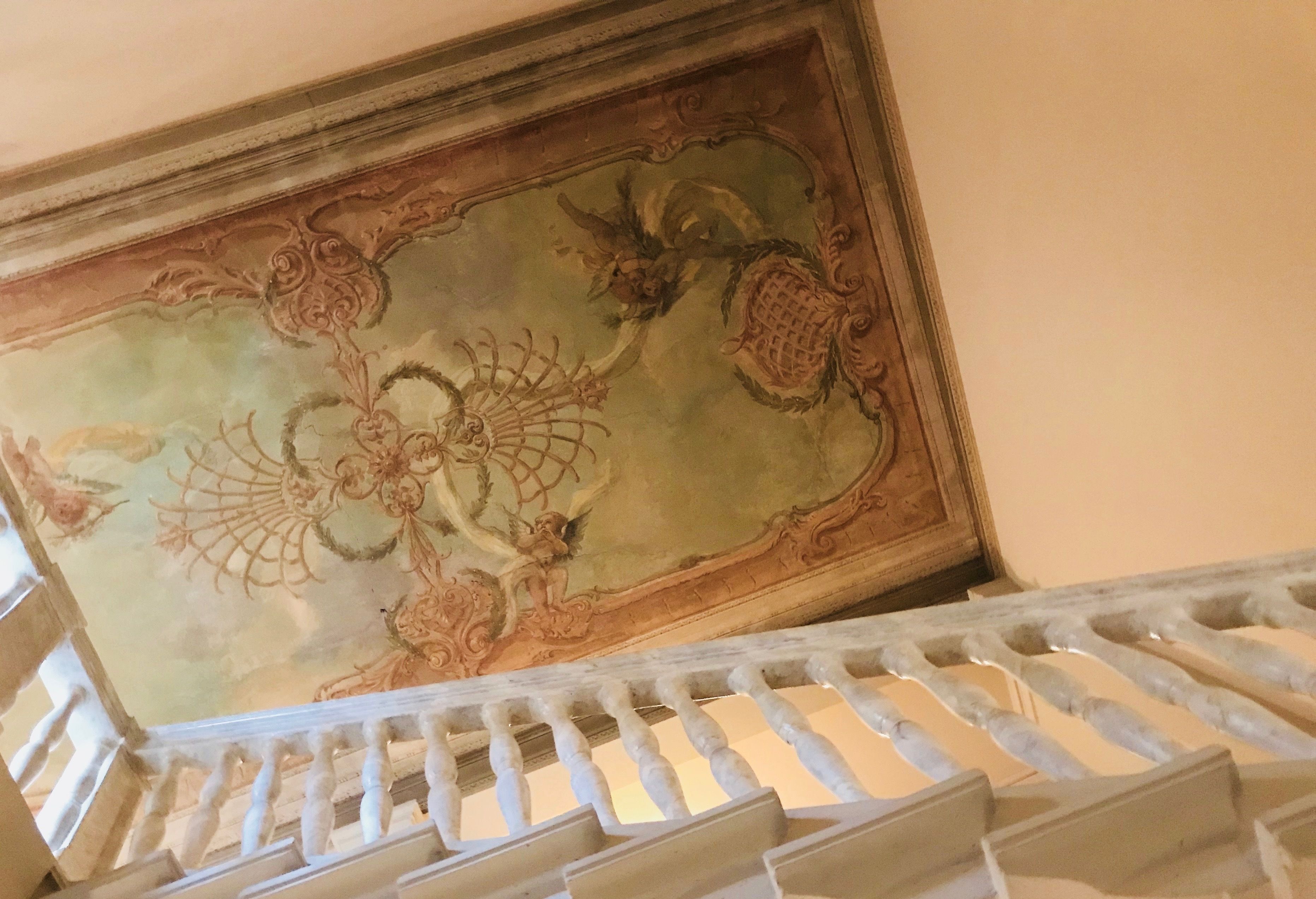 A staircase with a handrail and a decorative ceiling mural.