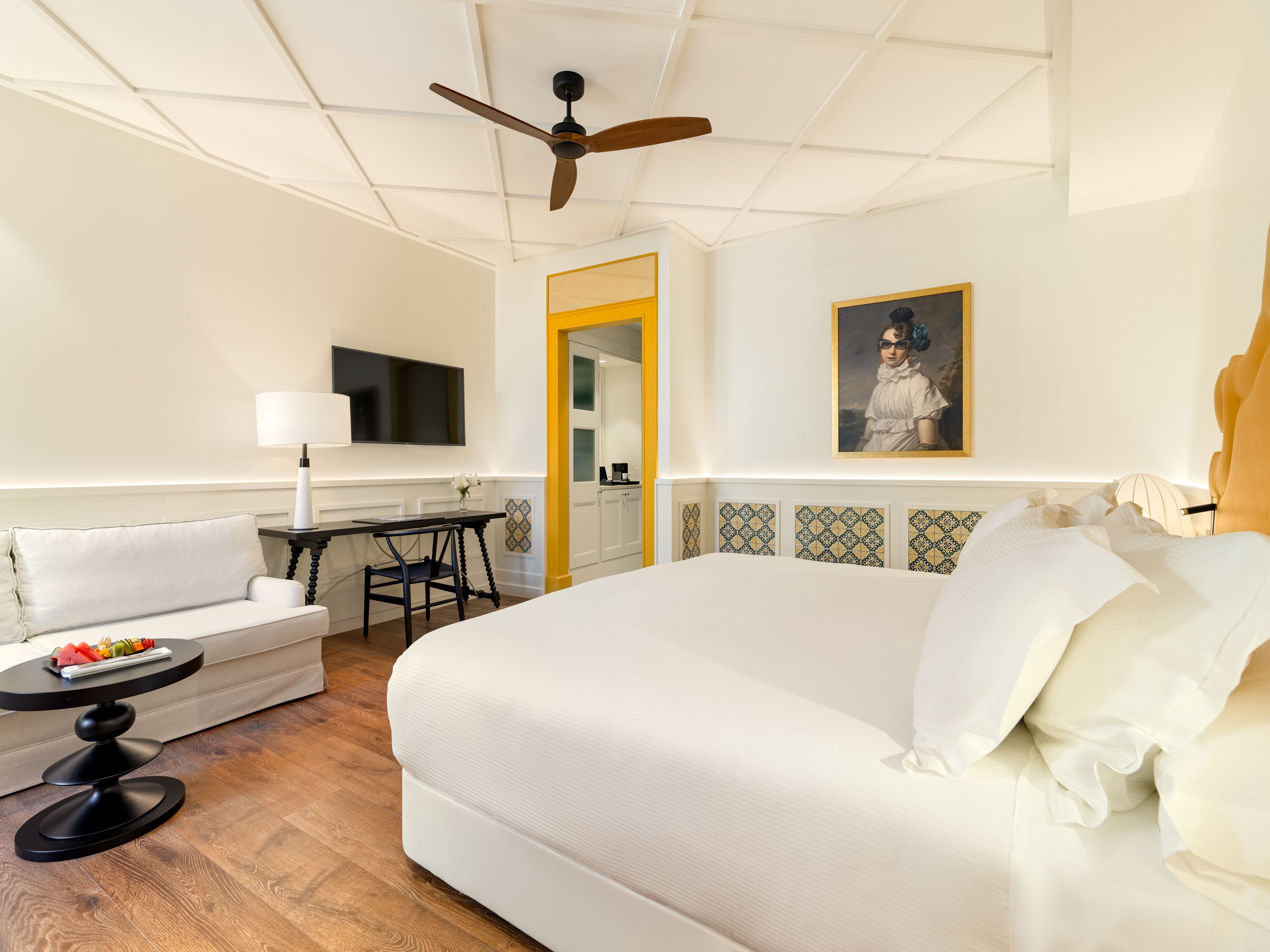 A hotel room with a large bed, a small table with a lamp, a sofa, and a ceiling fan.
