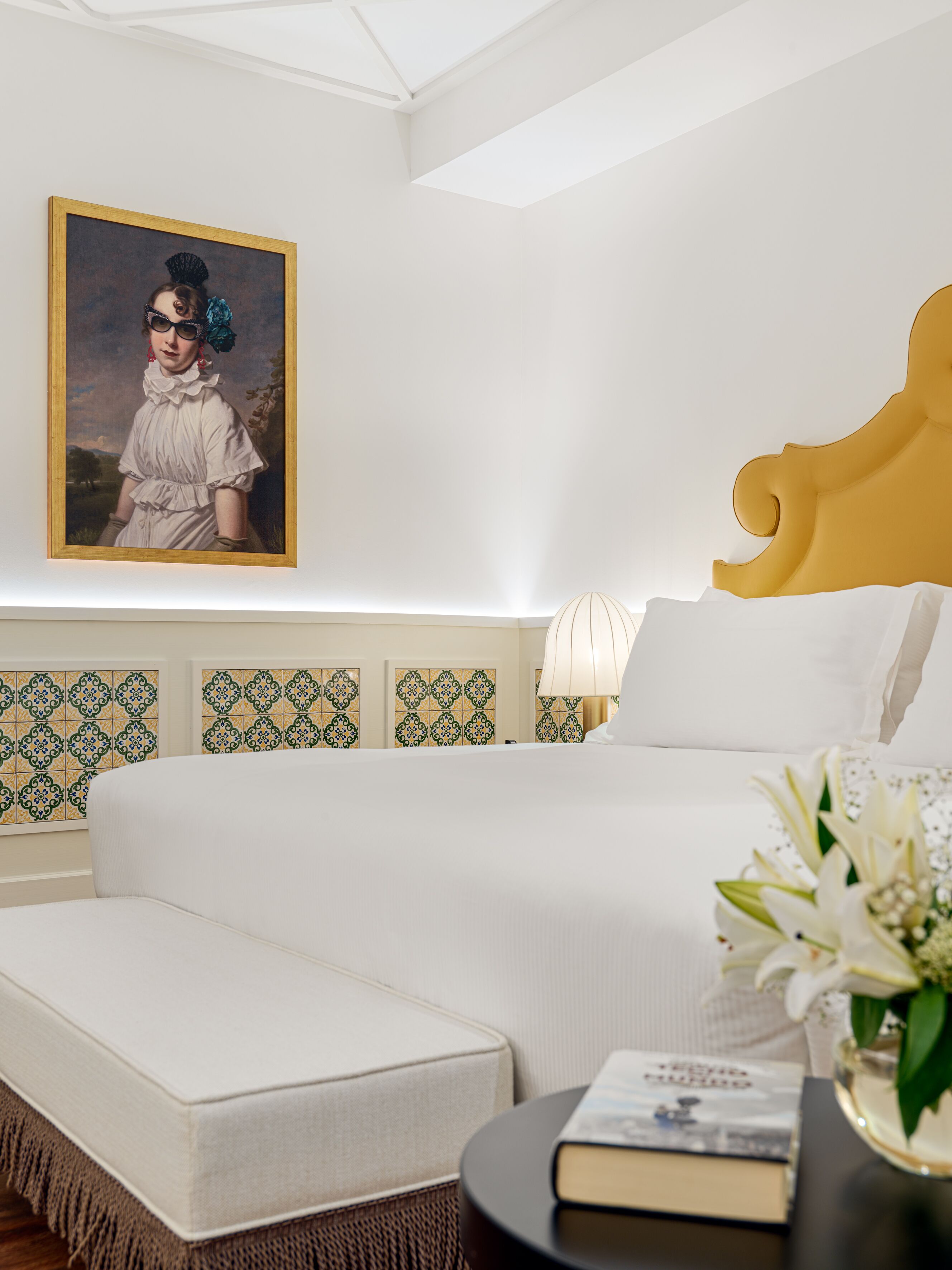 Habitación de hotel con cama, mesita de noche, lámpara, cuadro enmarcado y baldosas con diseño en las paredes.