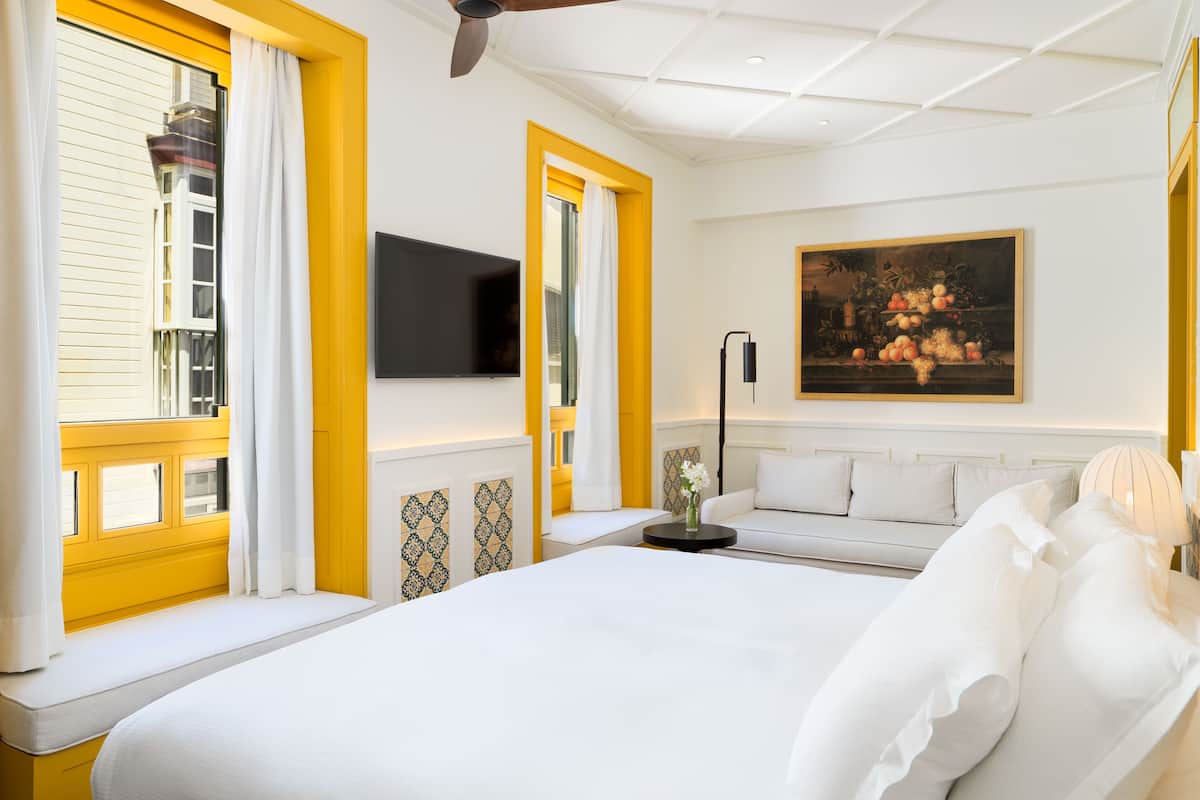 Une chambre d’hôtel avec un grand lit, un téléviseur à écran plat, un tableau et une fenêtre avec des bordures jaunes.