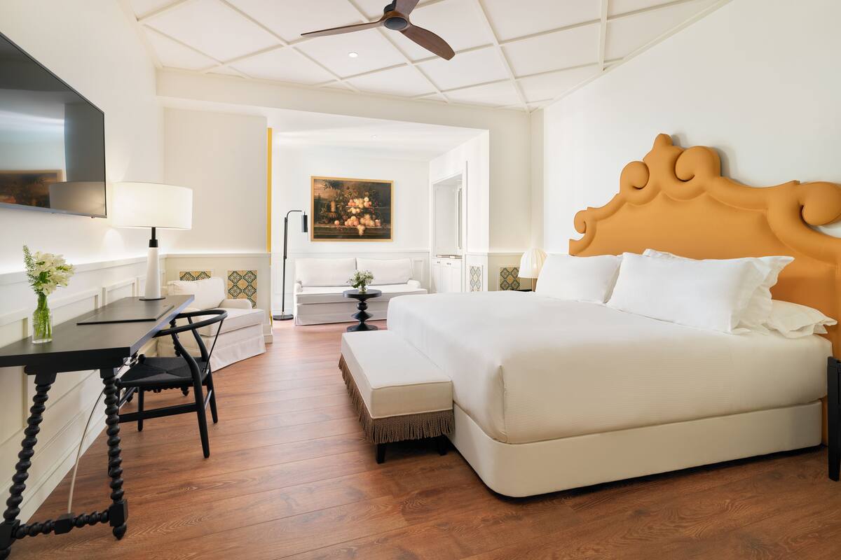 Une chambre d’hôtel avec un grand lit, un bureau avec une chaise, un téléviseur fixé au mur et un ventilateur de plafond.