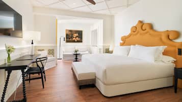Habitación de hotel con una cama grande, un escritorio con silla, televisor montado en la pared y ventilador de techo.
