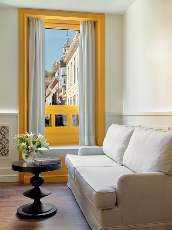 Una habitación con un sofá, una mesita con un florero y una ventana con cortinas.
