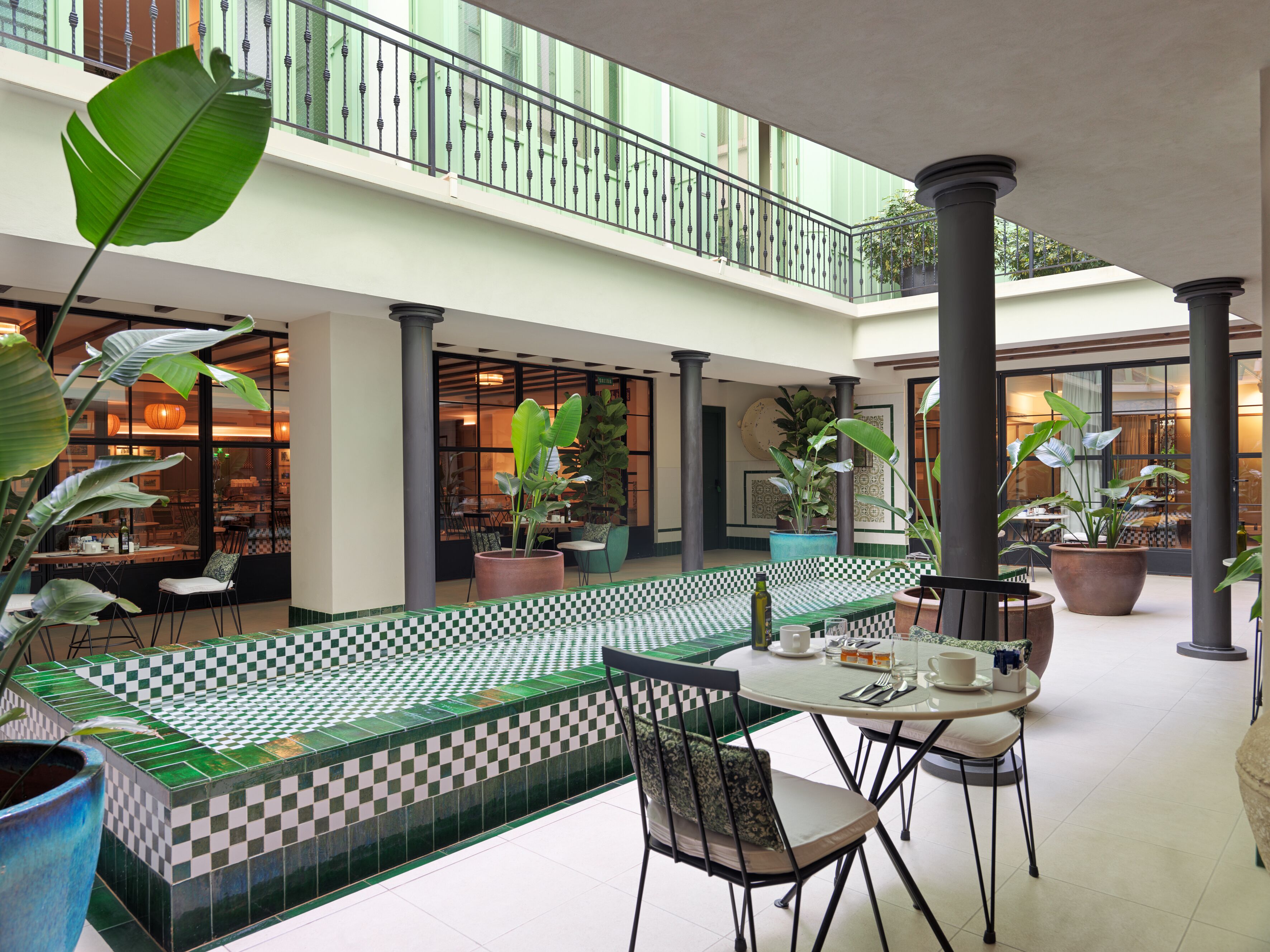 A spacious indoor area with a checkered floor, multiple seating arrangements, and large potted plants.