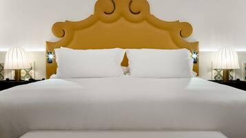 Een groot bed met een gouden hoofdeinde, witte lakens en twee bedlampjes.