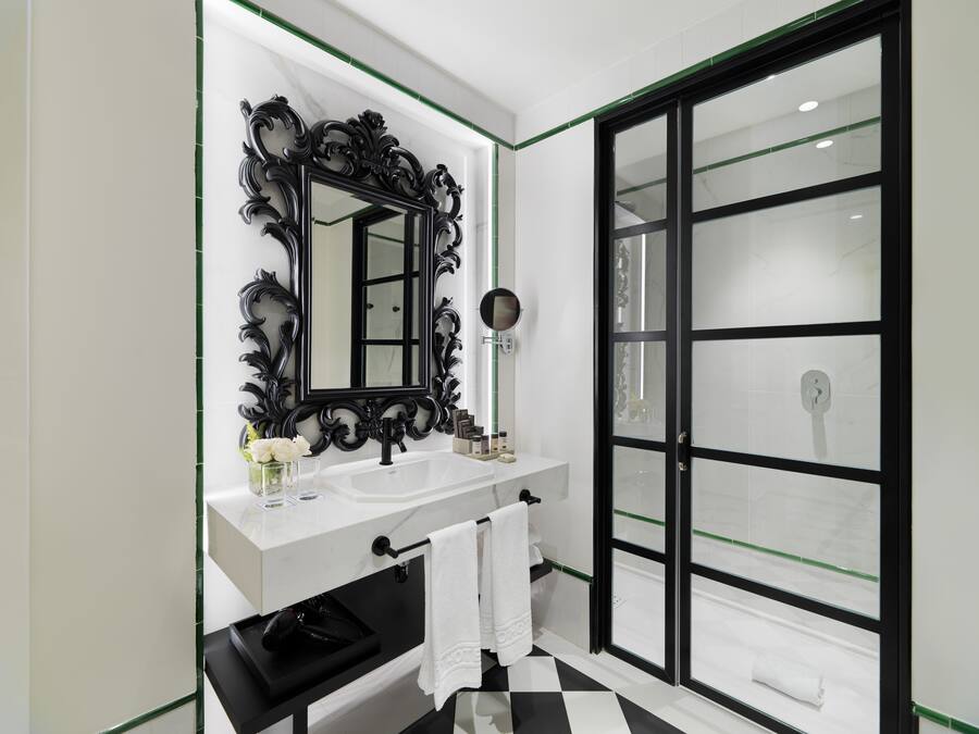 Een moderne badkamer met een grote spiegel, een witte wastafel, een zwarte wasbak en een douchecabine van glas.