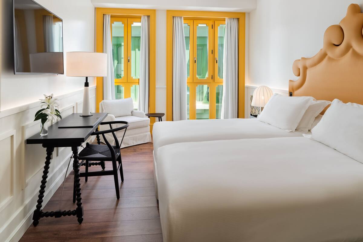 Une chambre d’hôtel équipée d’un lit, d’un bureau, d’une chaise, d’une télévision et offrant une vue sur l’extérieur.