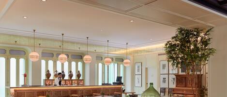 A spacious lobby with a checkered floor, wooden furniture, a bar area, and large windows allowing natural light.