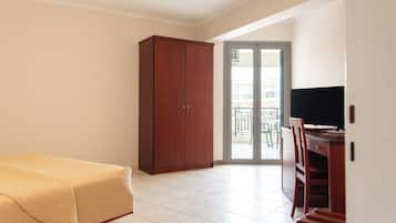 A bedroom with a bed, a wardrobe, a desk with a TV, and a sliding glass door leading to a balcony.