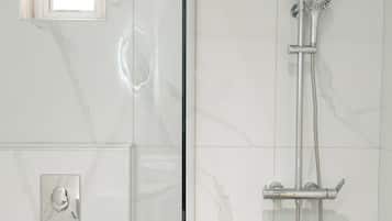 Un baño moderno con ducha acristalada, un ventanal pequeño y una toalla sobre una encimera blanca.
