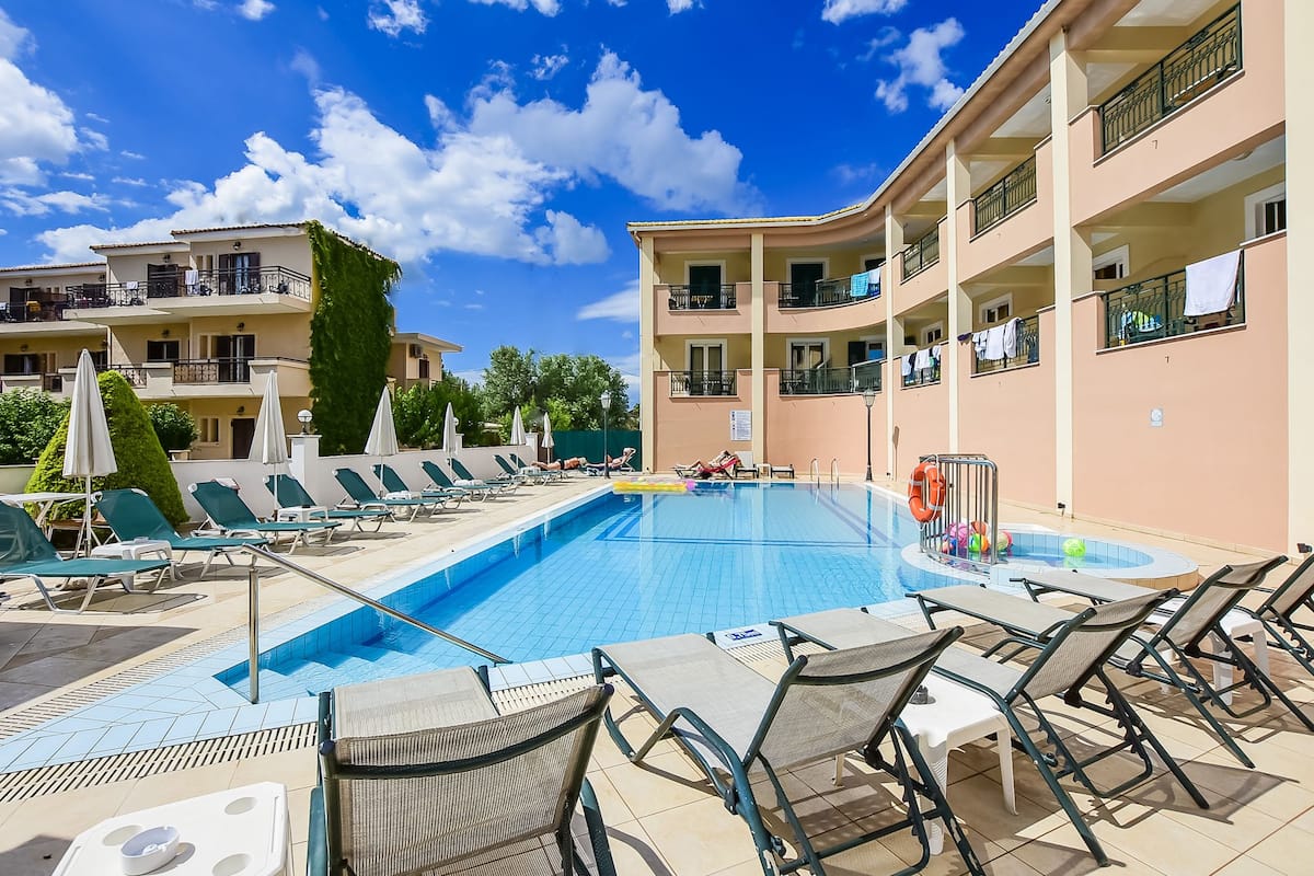 A swimming pool with lounge chairs and umbrellas, surrounded by multi-story buildings with balconies.