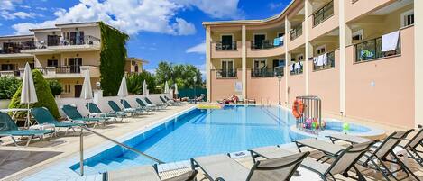 A swimming pool with lounge chairs and umbrellas, surrounded by multi-story buildings with balconies.