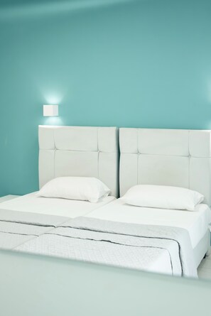 A bed with a white headboard and two pillows, set against a teal wall with a single bedside lamp. - Timos Hotel (Zakynthos)