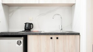A modern kitchen with a marble backsplash, a black electric kettle, and a stainless steel sink.