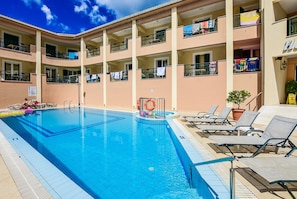 Un hotel de varios pisos con piscina, tumbonas y balcones donde se tiende ropa.