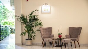 Un área de estar con dos sillones, una mesa, una planta en maceta y un cuadro en la pared.