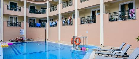 Un hotel de varios pisos con piscina, balcones y sillones de descanso.
