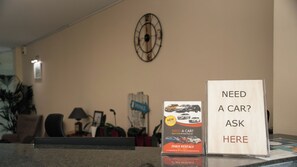 A reception desk with a clock on the wall, a sign offering car rentals, and a sign that reads 'NEED A CAR? ASK HERE'. - Timos Hotel (Zakynthos)