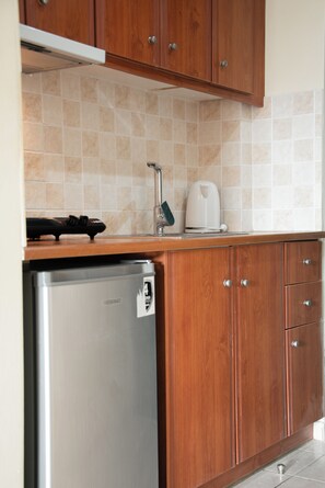 A kitchen with wooden cabinets, a stainless steel refrigerator, and a tiled backsplash. - Timos Hotel (Zakynthos)