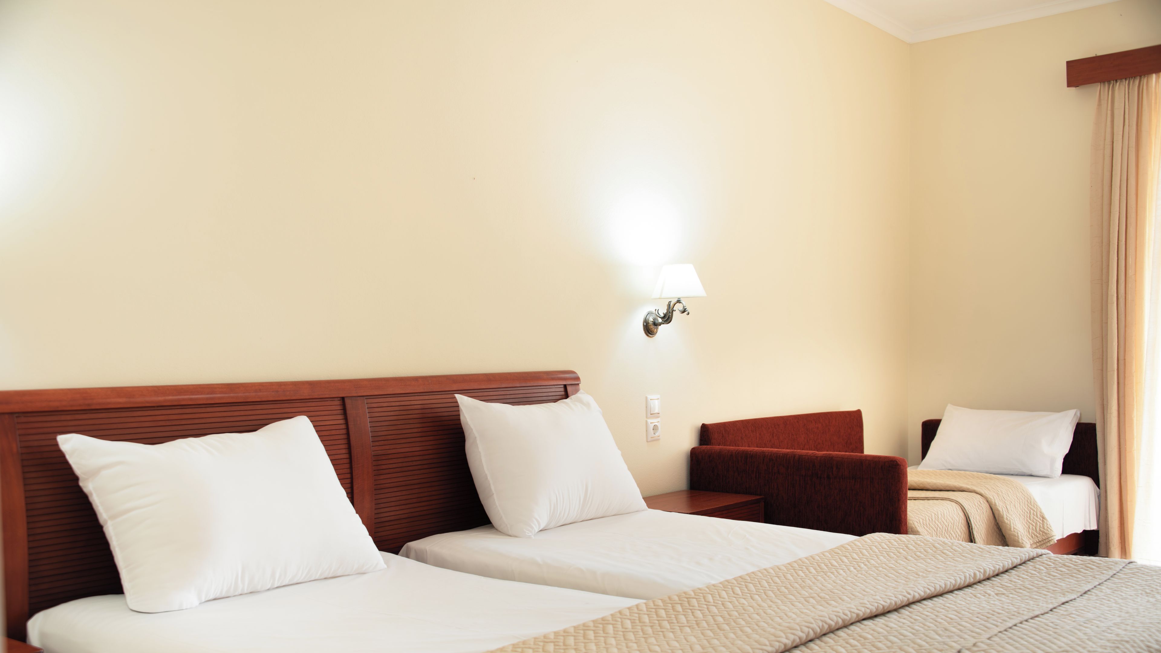 A hotel room with two beds, a nightstand, a lamp, and a window with curtains.