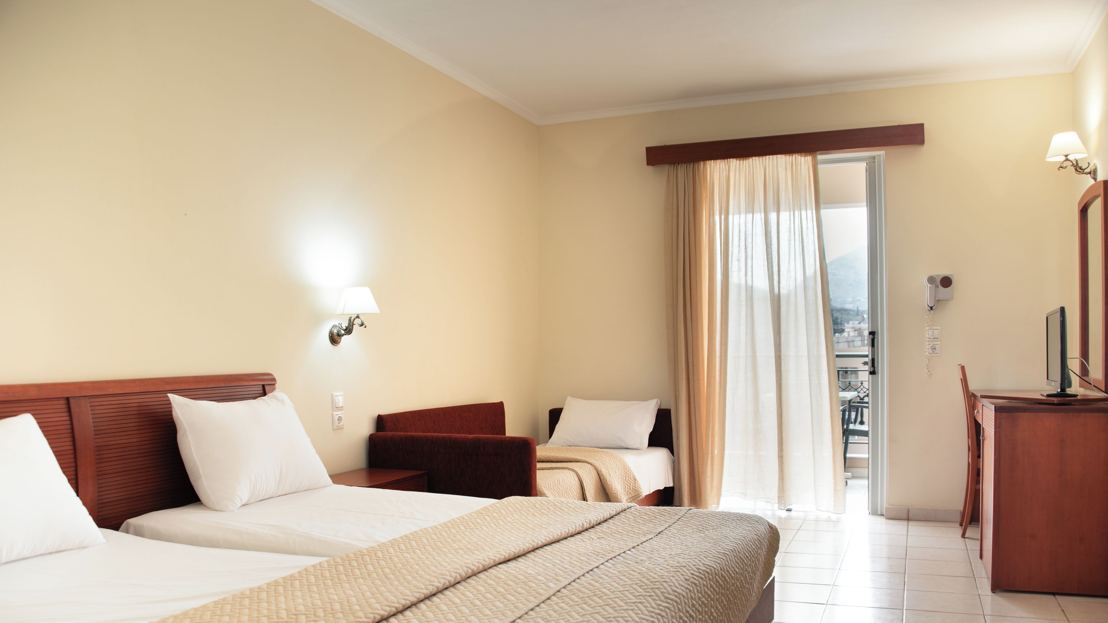 A hotel room with a bed, a desk, a chair, and a window with curtains.
