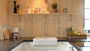 Una cocina con paredes de madera, un lavamanos blanco y una estufa. Hay estantes con frascos y una planta.