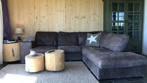 Una sala de estar con un sofá modular gris oscuro, dos taburetes de madera, una lámpara y un aparador verde con puertas de cristal.