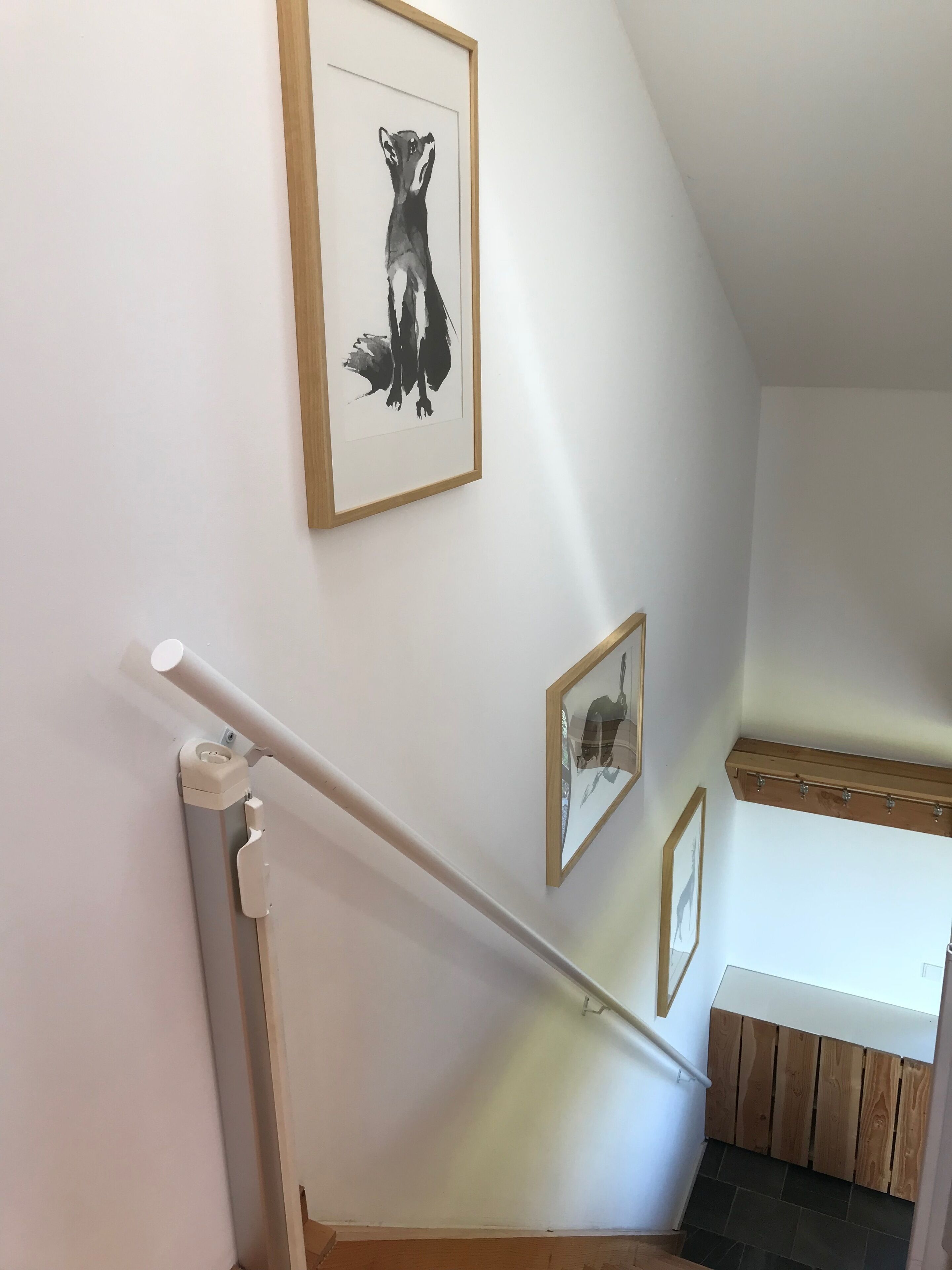 Una scala con corrimano, una stampa incorniciata di animali sulla parete e una panca di legno alla base.