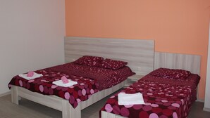 Quarto com duas camas, cada uma com colcha e almofadas listradas em vermelho e rosa.