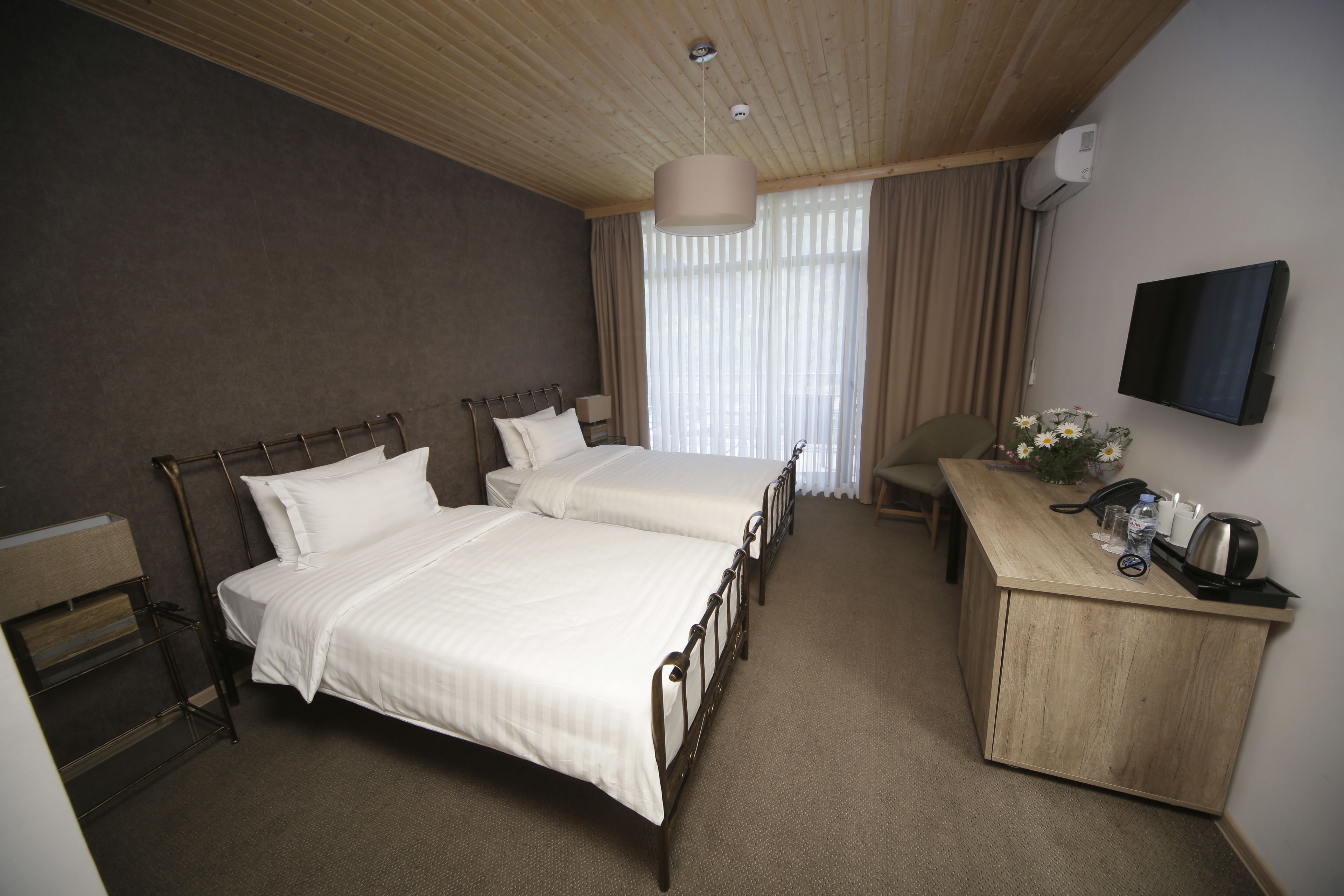 A hotel room with two beds, a desk, a chair, a TV, and a window with curtains.