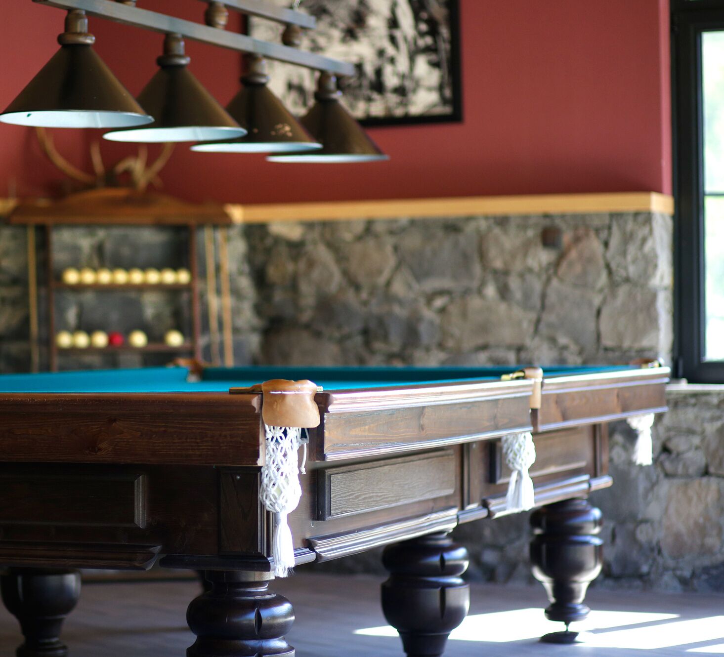 A pool table with a wooden frame and a cloth cover, positioned against a stone wall with a framed picture above it.