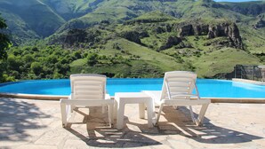 Zona de piscina con sillas y una mesa, con vistas a un paisaje montañoso.