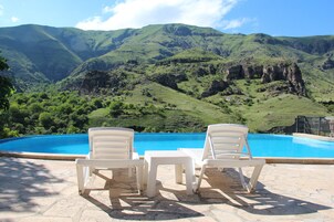 Zona de piscina con sillas y una mesa, con vistas a un paisaje montañoso.