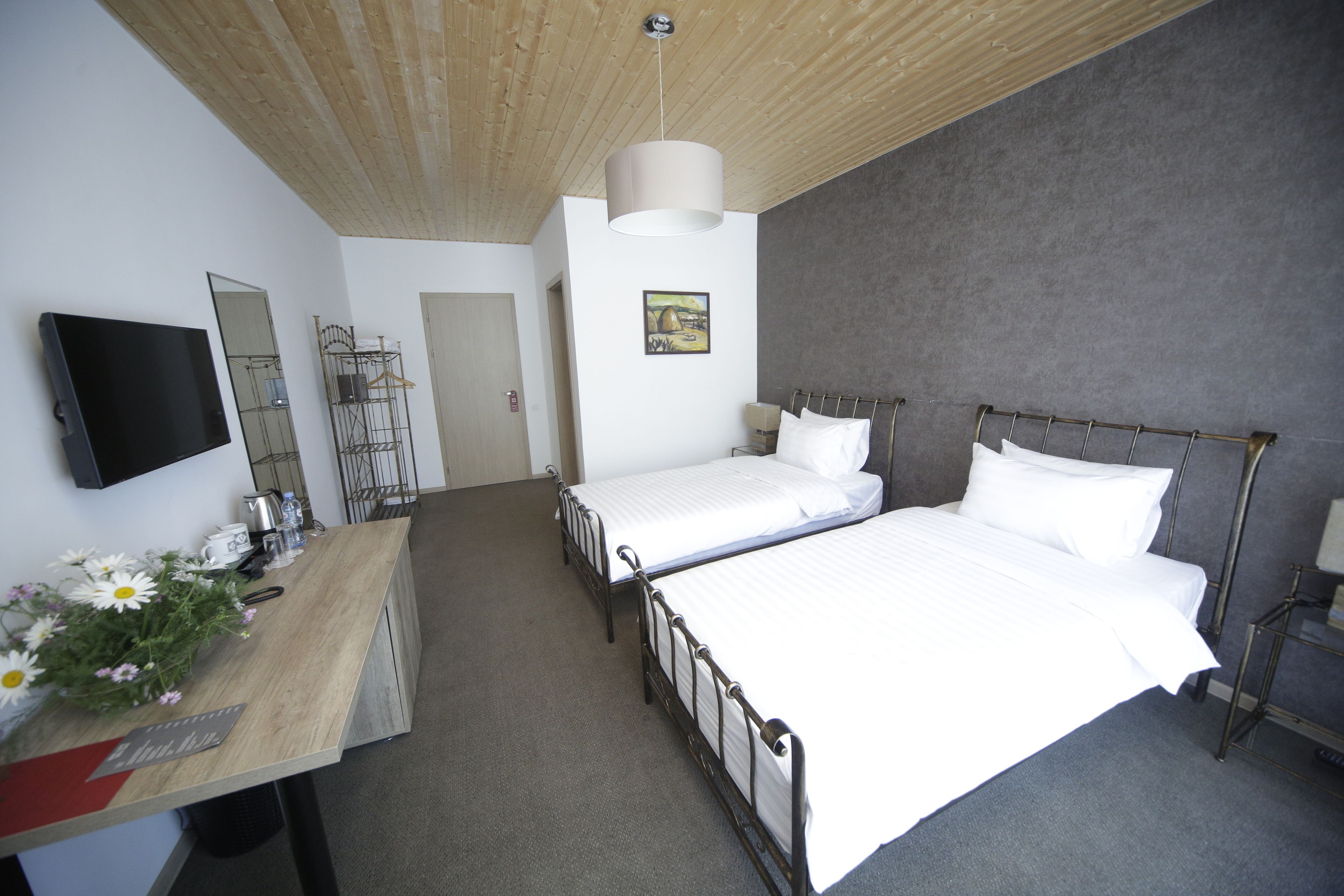 A hotel room with two single beds, a wooden desk with a flat-screen TV, a mirror, and a painting on the wall.