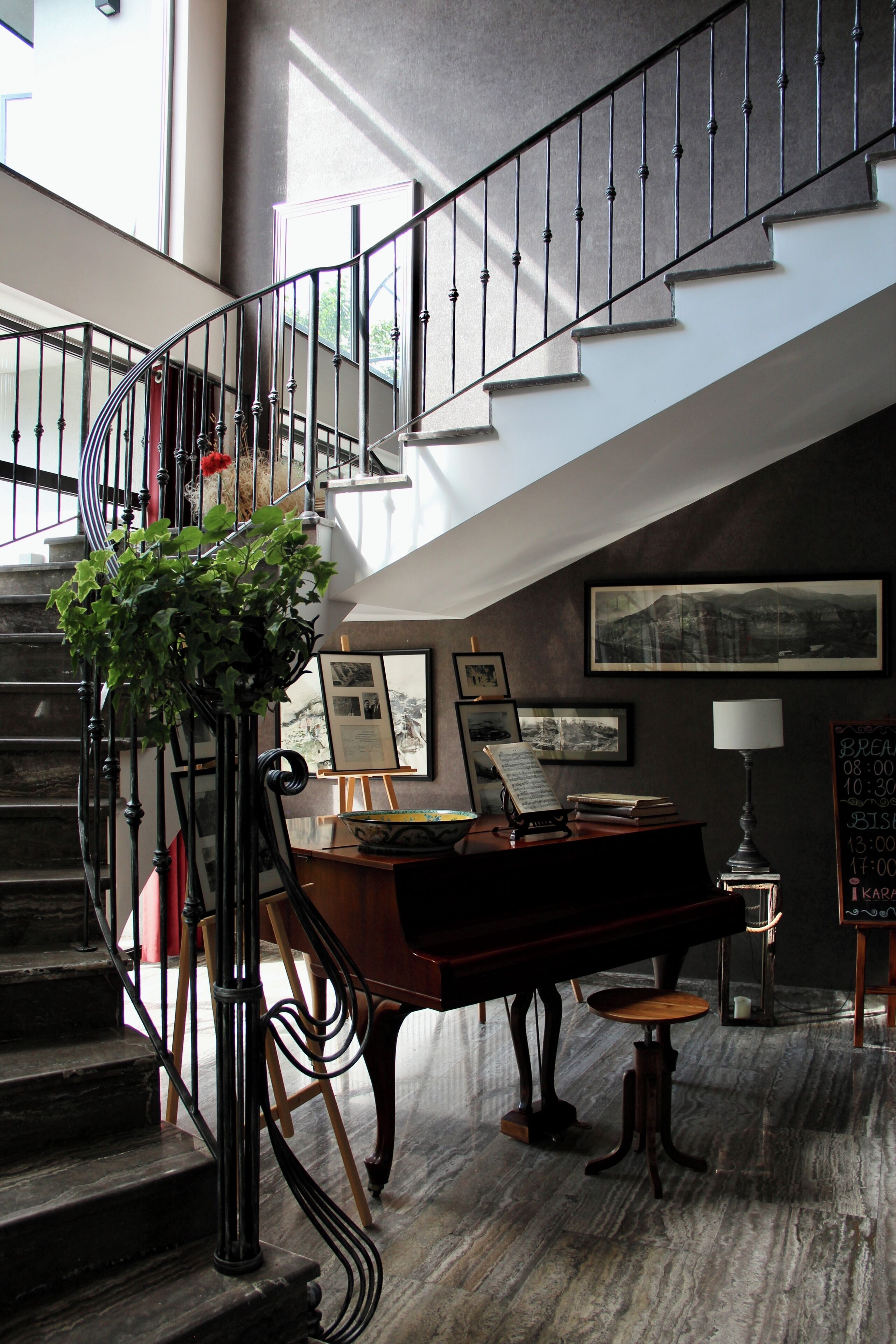 Eine prächtige Treppe mit einem Klavier und einem Esstisch, umgeben von gerahmten Bildern und einer Kreidetafel mit Speisekarte.