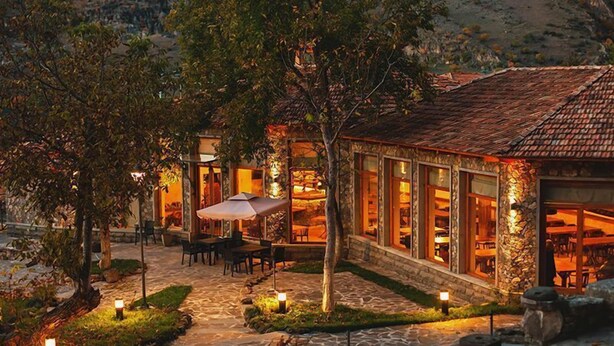 Un edificio de piedra con tejado de tejas, mesas al aire libre y ventanas iluminadas.