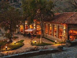 Un edificio de piedra con tejado de tejas, mesas al aire libre y ventanas iluminadas.