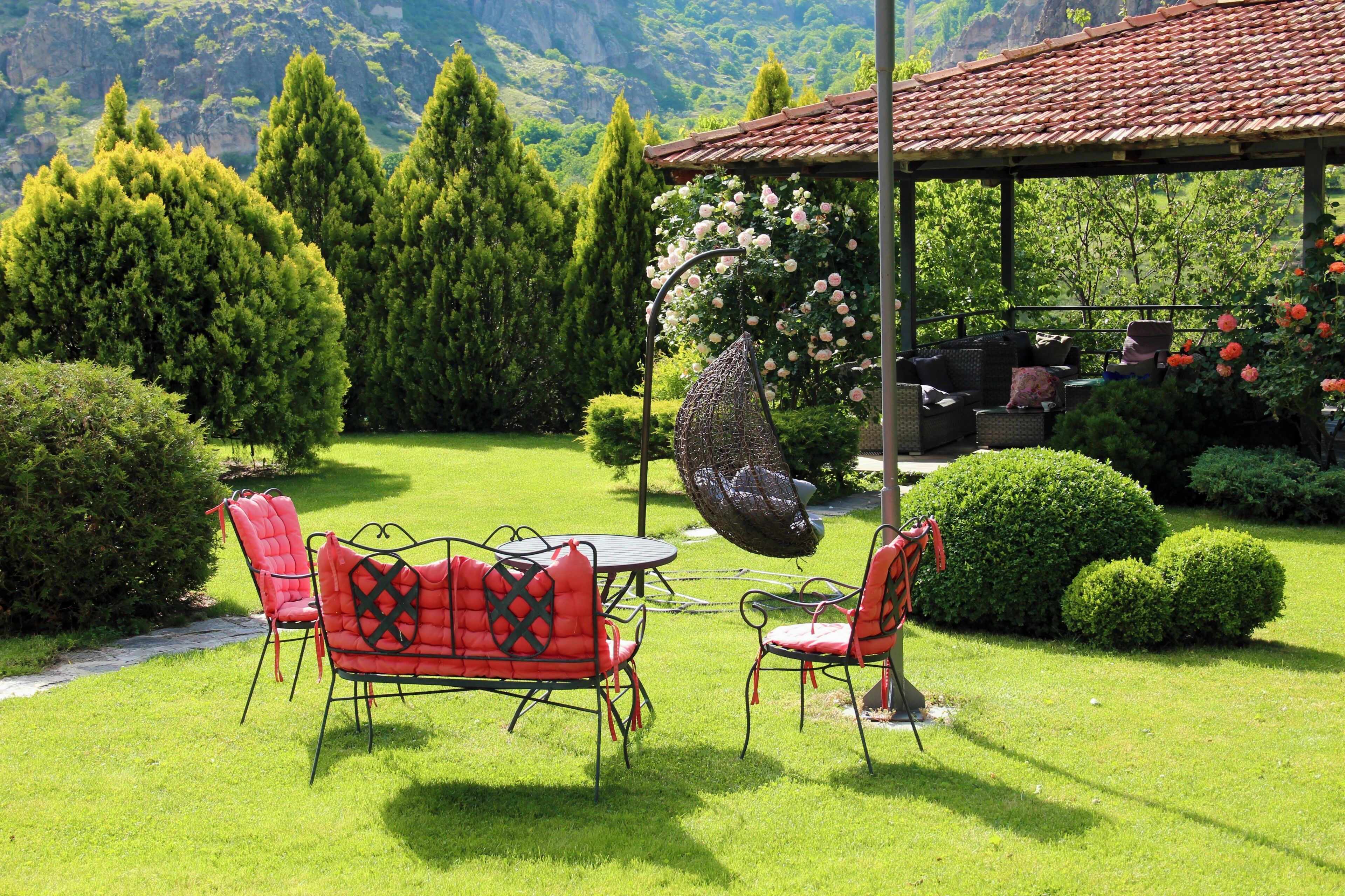 A garden with a pergola, red chairs, a table, and a hanging bird feeder.