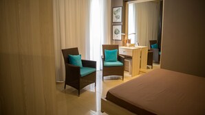 Ein Hotelzimmer mit einem Bett, zwei Korbstühlen mit türkisfarbenen Kissen, einem Schreibtisch mit einer Lampe und einem großen Spiegel.