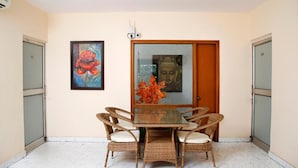 A dining area with a glass-top table, wicker chairs, and a Buddha statue in the background. - Maplewood Stay (New Delhi)