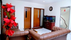 A living room with brown leather sofas, a wooden cabinet, and a television. - Maplewood Stay (New Delhi)