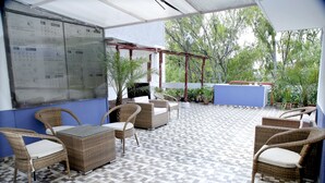 A covered patio area with wicker furniture and a tiled floor. - Maplewood Stay (New Delhi)