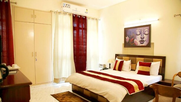 A hotel room with a bed, a desk, a chair, a wardrobe, and a painting on the wall. - Maplewood Stay (New Delhi)