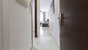 A hallway with a white wall, a wooden door, and a bench in the distance. - Apartamentos El Tajo (Ronda)