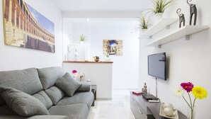 A modern living room with a grey sofa, a flat-screen TV, and decorative items including flowers and figurines. - Apartamentos El Tajo (Ronda)
