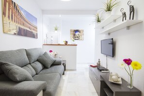 En moderne stue med en grå sofa, et fladskærms-tv og dekorative elementer, herunder blomster og figurer.